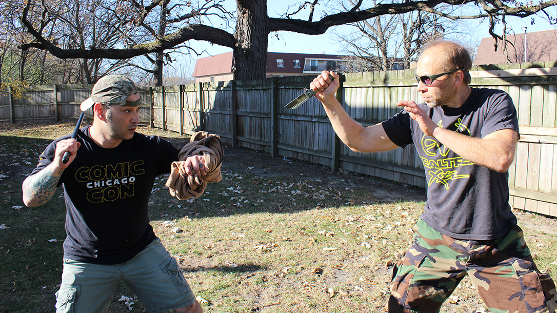 The author uses a wrapped jacket around his arm to protect himself from being cut. He uses a fighting stick as an equalizer for knife defense.