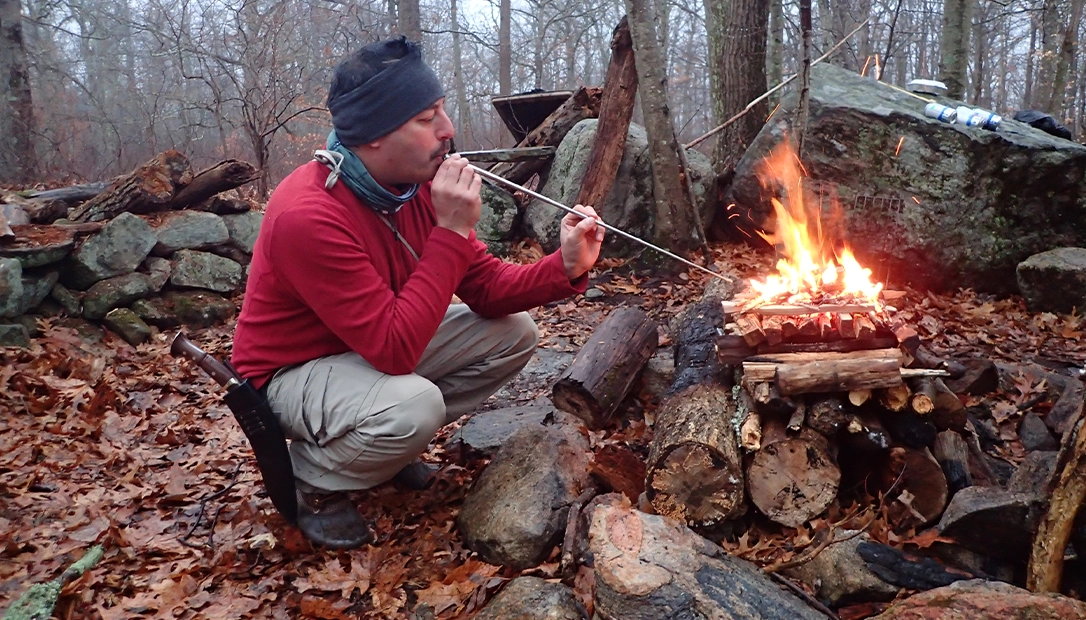 The author uses a fire bellows to breathe life into a winter pyramid fire. It served as the cook fire and warming fire in cold winter weather.