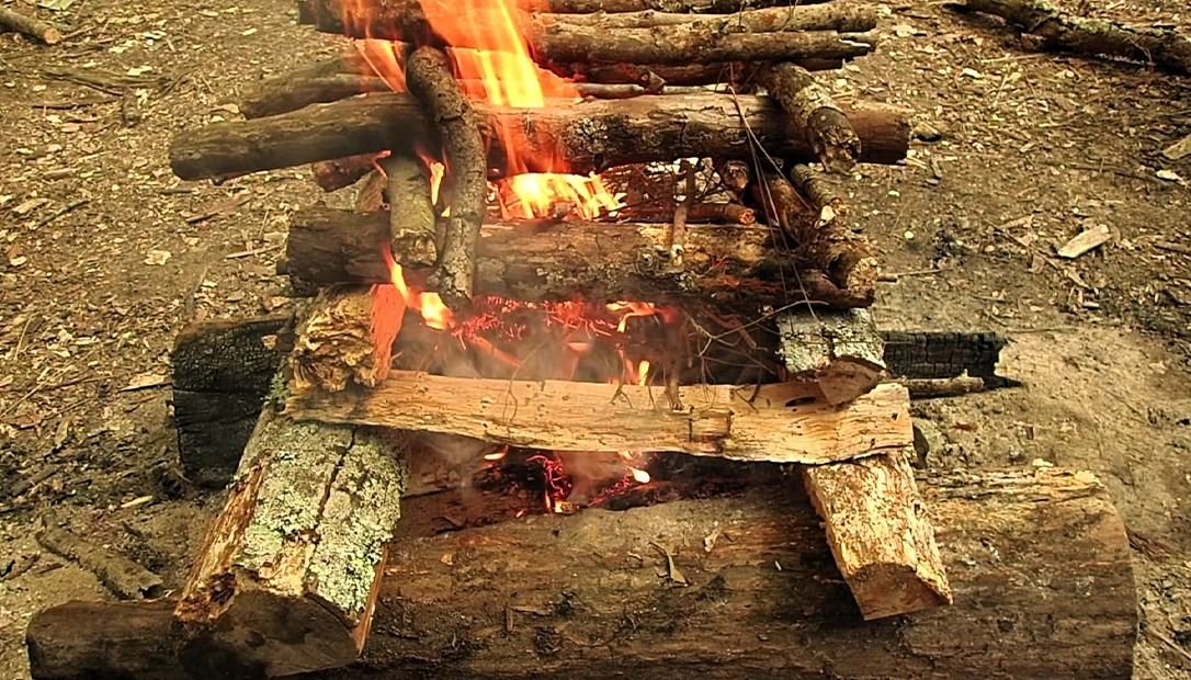 A large, waist-high log cabin fire lay was made with thick hardwood. It was ignited from the bottom on dry ground and utilized the hot rising airflow.