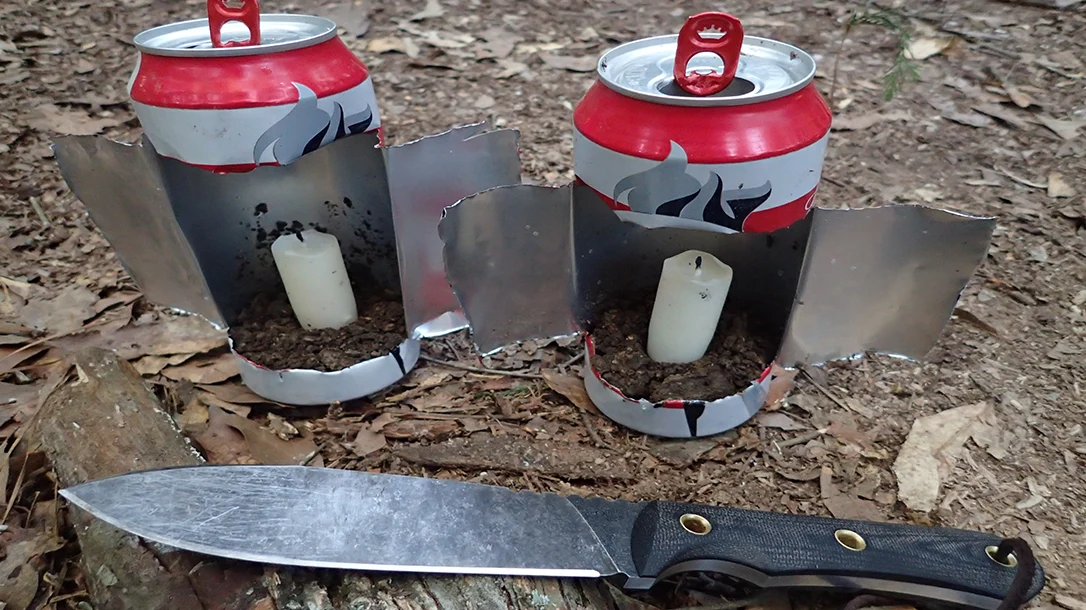 Two discarded beer cans were turned into camp lanterns by cutting an "H" shape and unfolding them, with adjustable wings for wind protection.