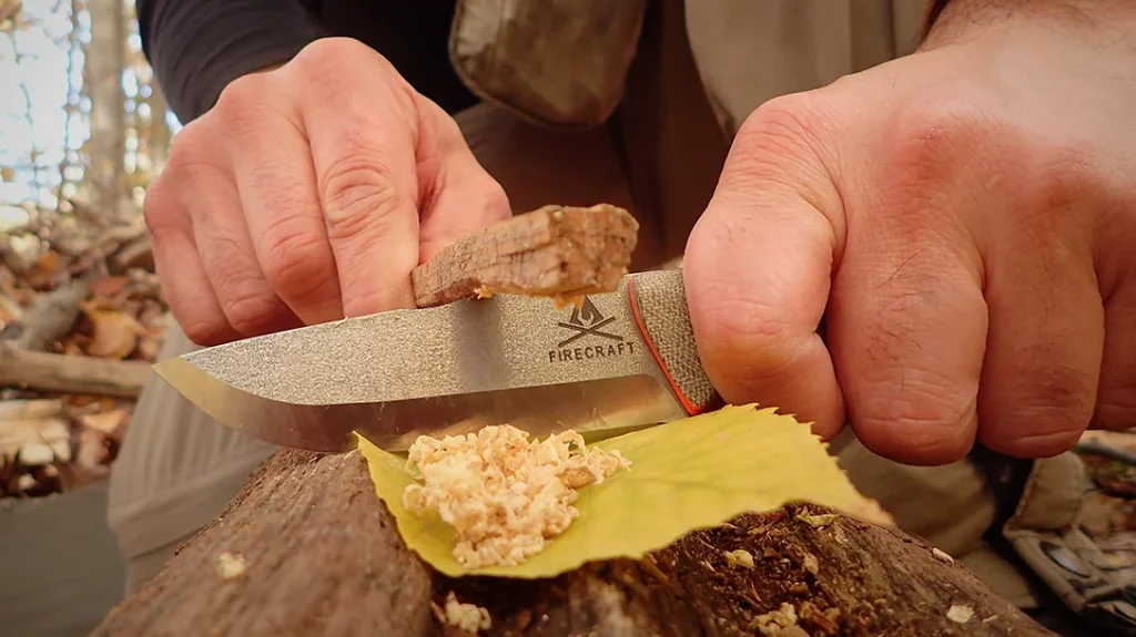 The knife is fixed in a horizontal position, and fatwood is scraped against the sharpened notch to get a pile of shavings.