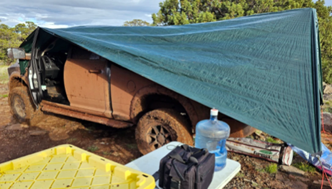 A tarp stretched from the truck to nearby tie-off points created an improvised shelter on the exposed granite campsite.